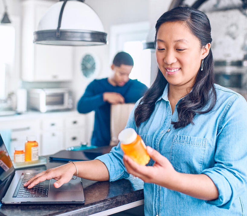 Señora sosteniendo un frasco de pastillas en una computadora portátil